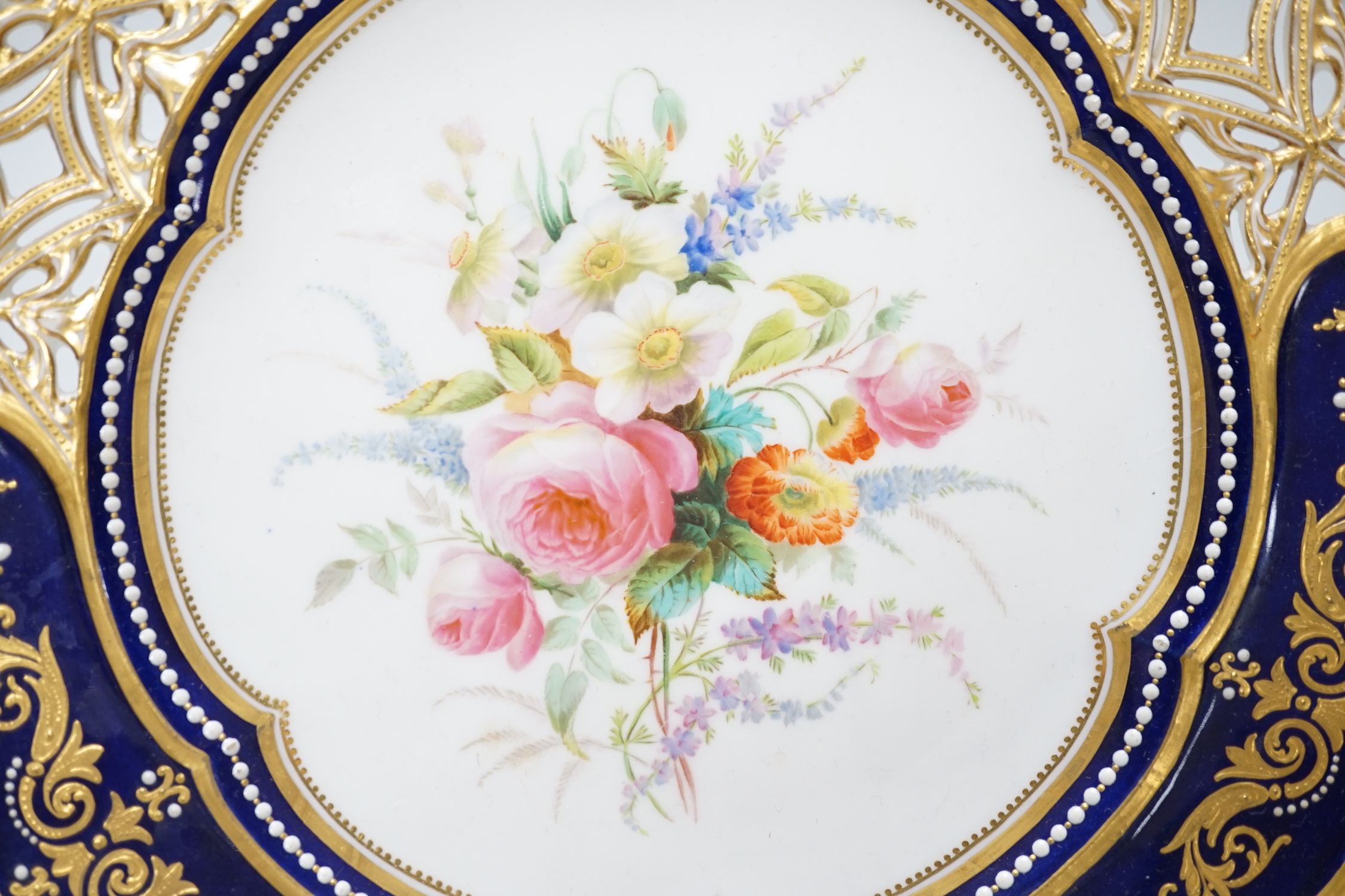 A Coalport plate with pierced border enamelled with white flowers and neo-classical raised paste gilding, the centre painted with bold flowers under jewelled inner border, ampersand mark